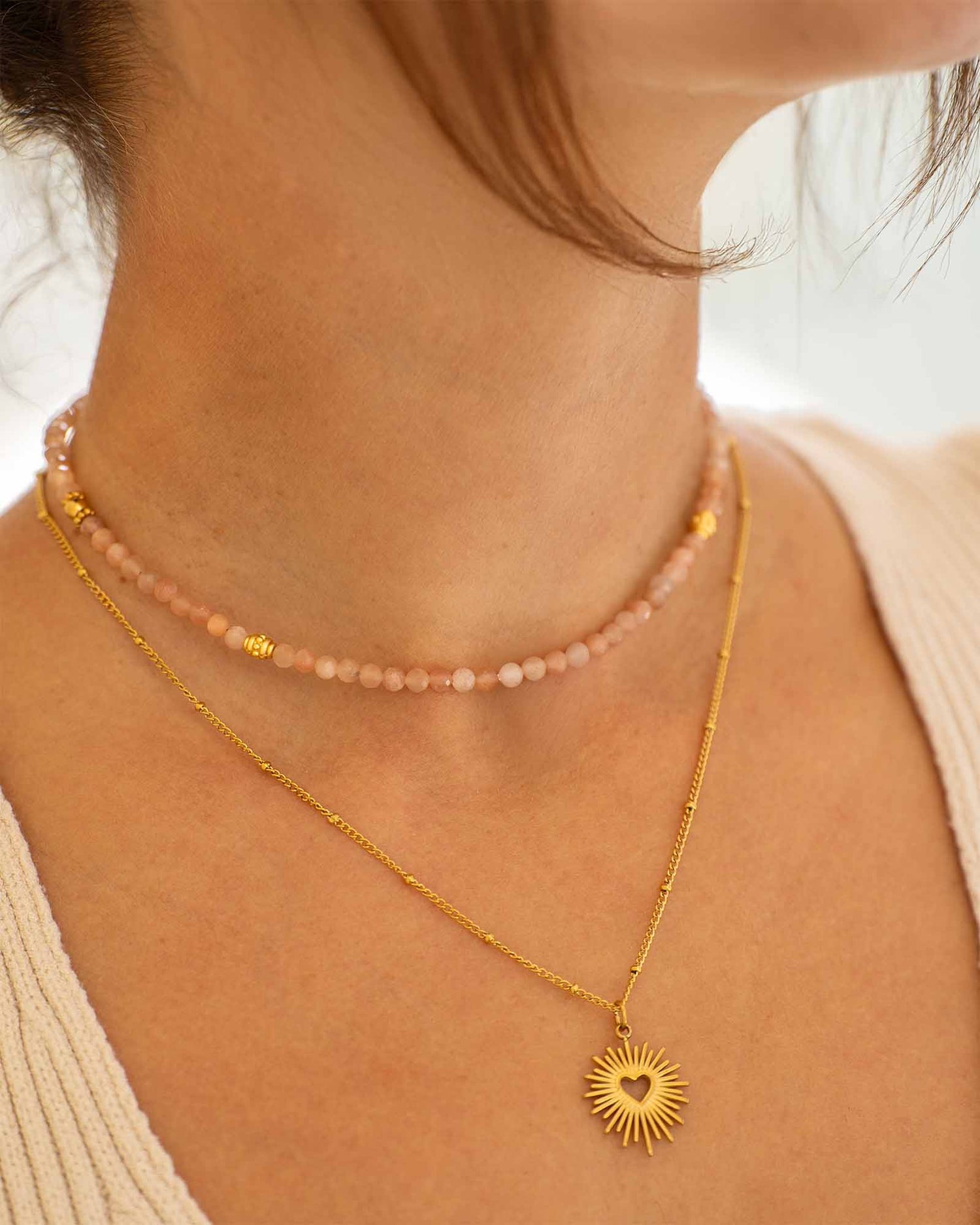 Frau trägt vergoldete Halskette mit Herz Sonnen Anhänger und Naturstein Halskette mit Sunstone